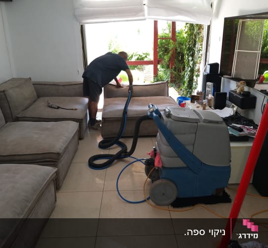 אדם מנקה ספה עם מכונת ניקוי מקצועית